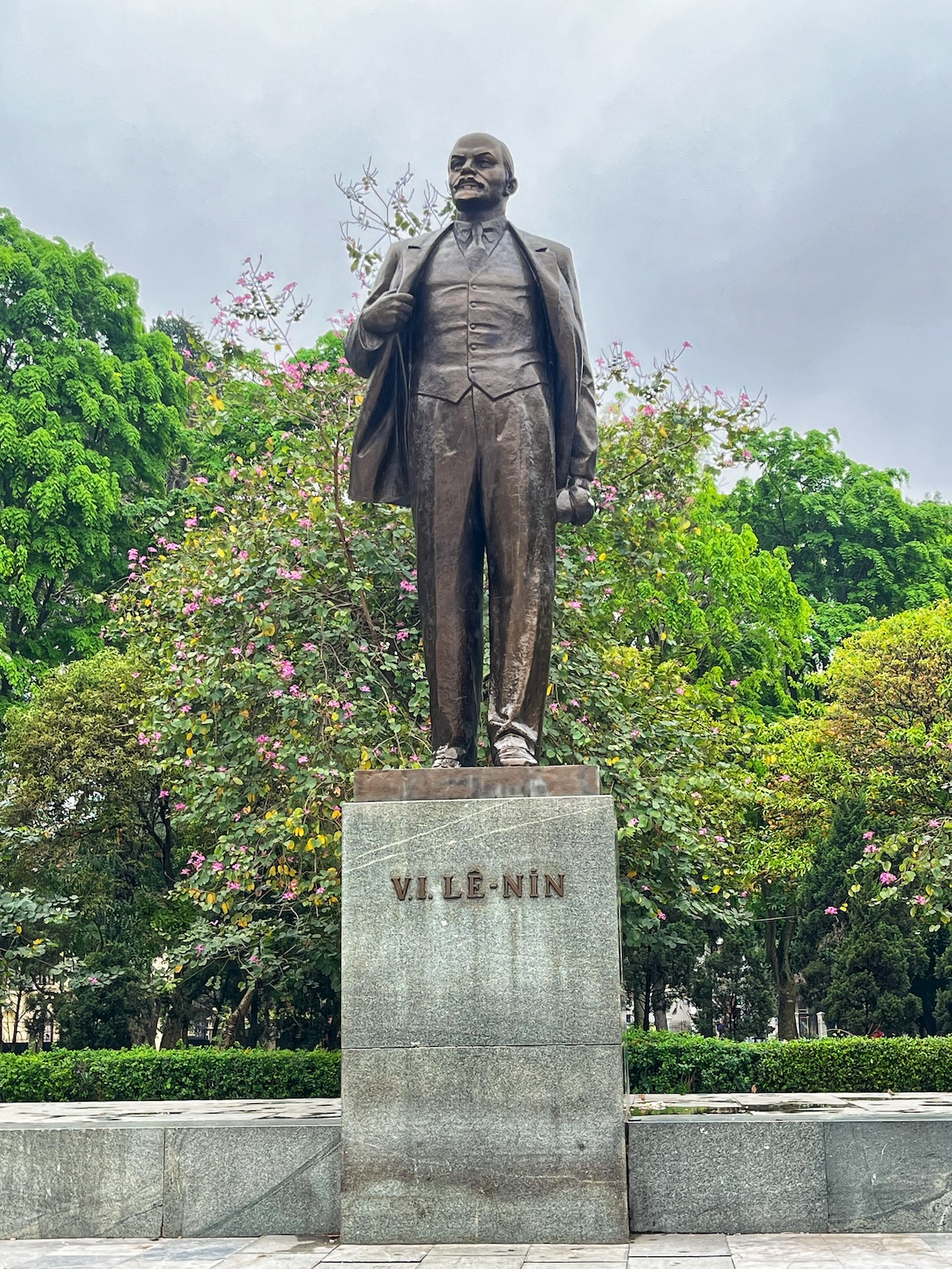 A bronze statue of Vladimir Lenin in front of green trees