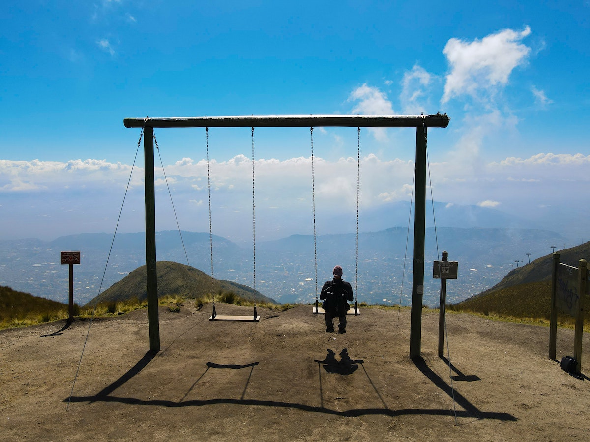 A tourist sits on a giant swing facing a mountainous city centre.
