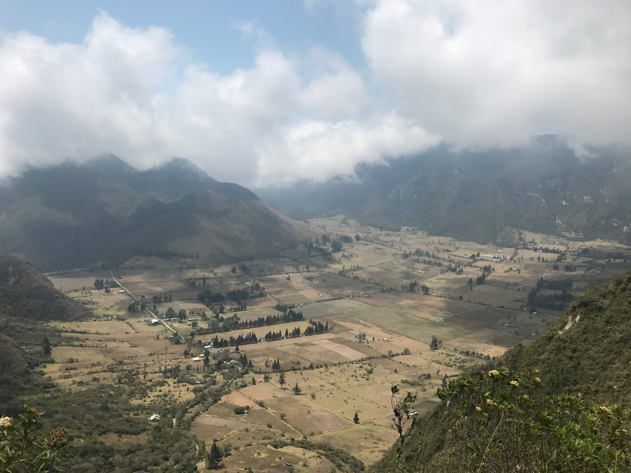 Misty clouds overlook large green mountains and fields in Quito, Ecuador.