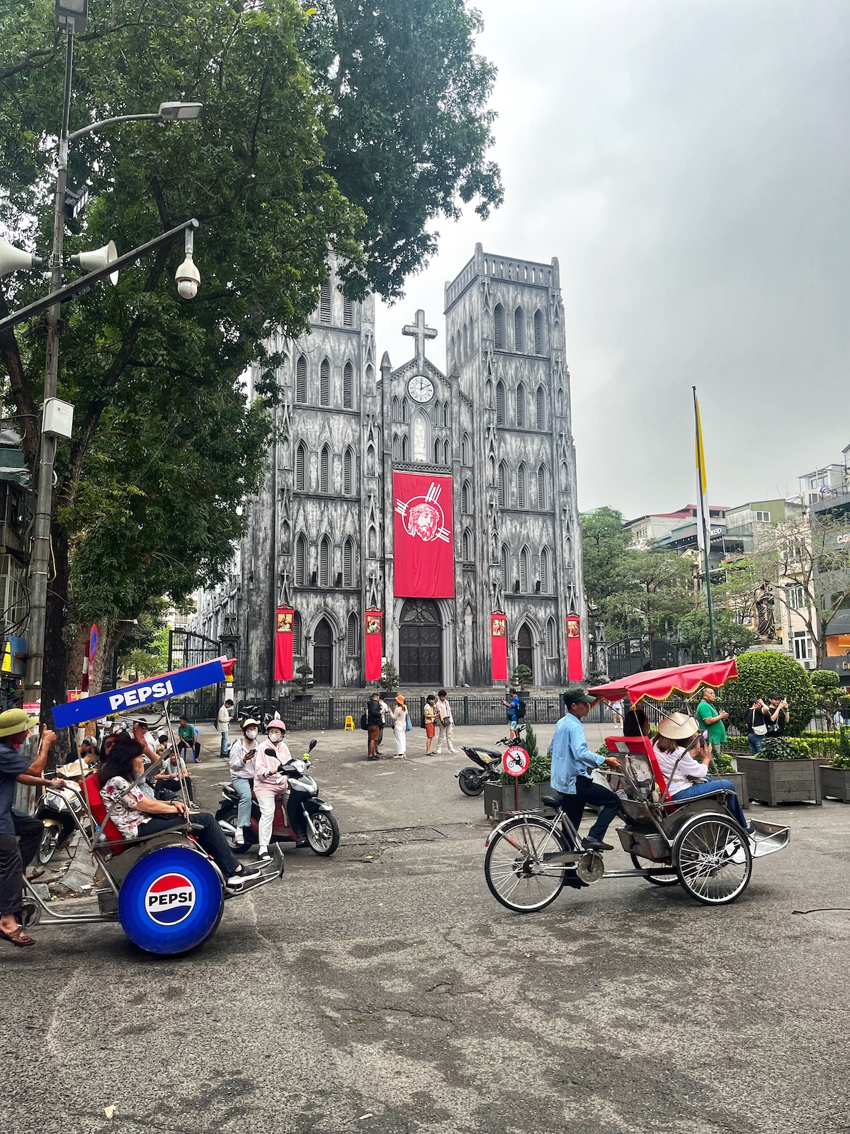 A grey gothic building with red decorations in front of busy traffic in central Hanoi, Vietnam