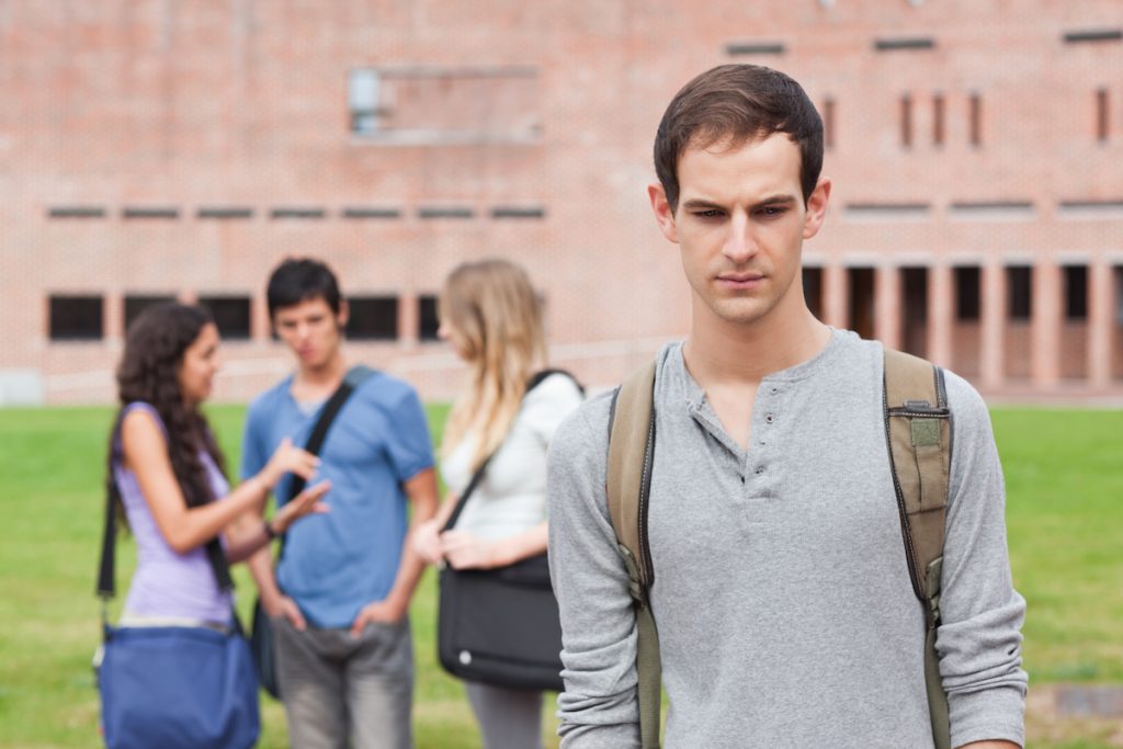 A man is lonely in a crowd while his classmates are talking outside a building