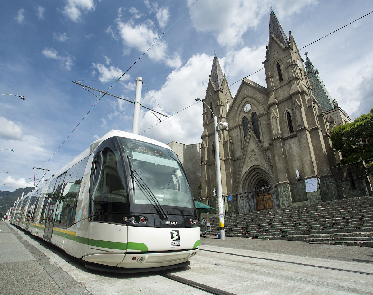 11 Honest Reasons To Learn Spanish in Medellin, Colombia • public transportation in medellin A tram passes a small church in Medellin, Colombia