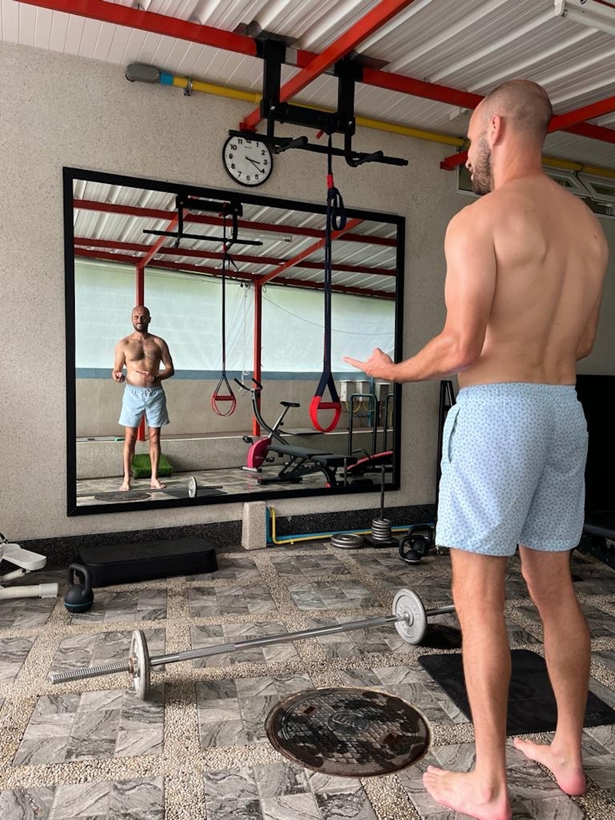 Shirtless man stands in front of the mirror in between sets lifting weights